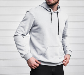 Man wears white hoodie. Bearded young sporty guy is standing in light fleece long sleeve sweatshirt