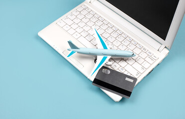 White laptop on a blue background. Nearby is a bank card and a miniature airplane. Concept - Online booking of air tickets, travel planning. Payment for orders via the Internet.