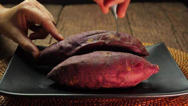 Hand cut and open up baked sweet potato closeup, Japanese Roasted Sweet Potato on wooden table in garden.