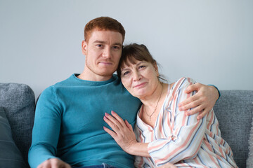 Cheerful elderly woman sitting on the sofa next to his adult son. caring son hugs his elderly mother. relations between different generations.