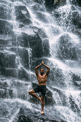 A man of athletic build does yoga. Healthy lifestyle. The concentration of the body. A man does yoga at a waterfall. A man does yoga in Bali. A man meditates in nature. Meditation at the waterfall