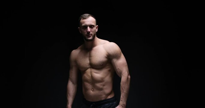 Shirtless muscular man posing with arms akimbo over black background