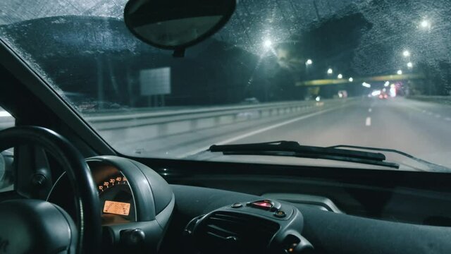 Close-up, interior of moving car along night highway, view through windshield. Road in blur, bokeh from headlights of oncoming cars, lanterns on track. Auto driving on freeway with high speed evening