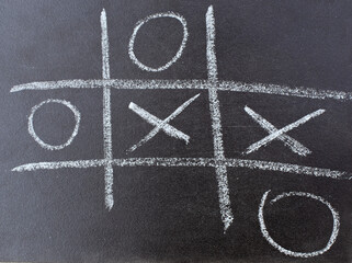 The tic tac toe game on blackboard with chalk grid, naughts and crosses