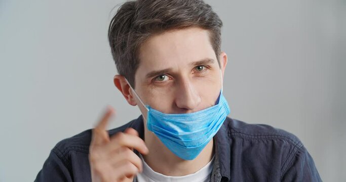Portrait of responsible man looking at camera demonstrates how to properly wear medical face mask by closing his mouth and nose teaches safety rules and social norms during pandemic showing thumbs up