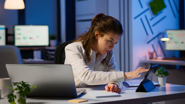 Manager woman using laptop and tablet in same time working overtime in business start-up office. Busy multitasking employee using modern technology network wireless overworking writing, searching.