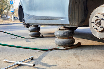 Car without wheels lifted up with jacks during wheel replacement. Seasonal change of car tires.