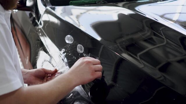 Paint protection film Installation on a black car. Master applies polyurethane protective film using squeegee tool to remove excess water from under the film surface close-up