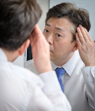 Asian Middle-aged Man Looking In The Mirror And Touching His Hair