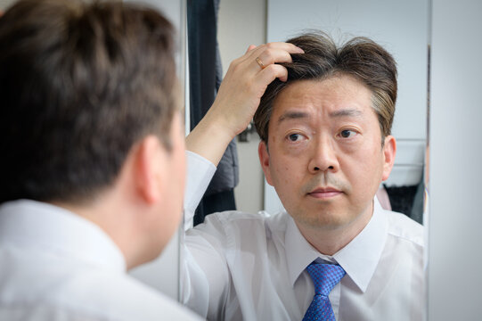 Asian middle-aged man looking in the mirror and touching his hair