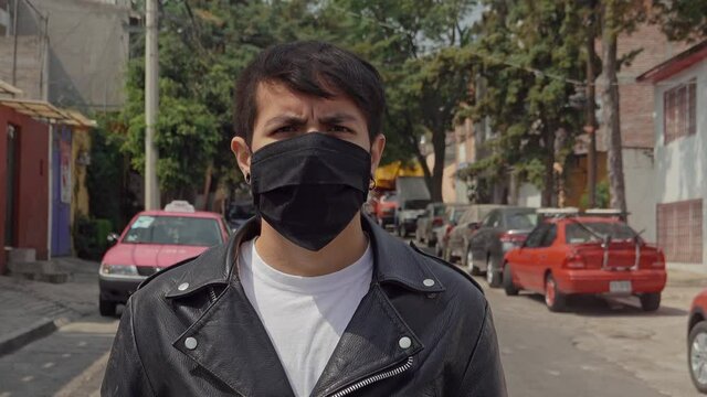 Portrait Of A Latino Young Male Punk Rocker Adult Taking Off A Black Face Mask Standing On The Street And Wearing Leather Jacket During Covid-19 Pandemic 