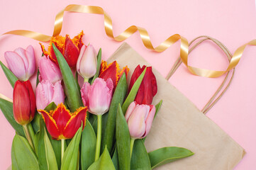 Bouquet of pink and red tulips and a paper bag on a pink background.