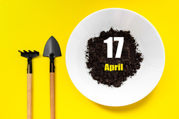 April 17th. Day 17 of month, Calendar date.White plate of soil with a small spatula and rake on...