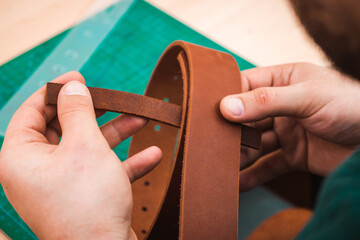 Hands sew a brown belt with threads and a needle