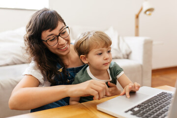 Fototapeta na wymiar Mãe autônoma e filho sorrindo trabalhando no computador em casa