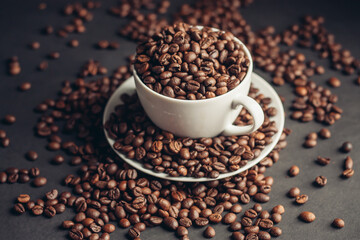 saucer with coffee beans and white cup on gray table close-up