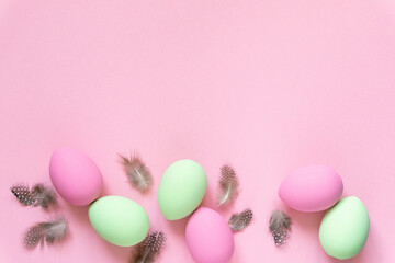 Flat lay of pink and green easter eggs with feathers on pastel background, space for text