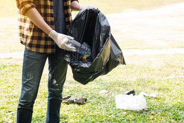 Man's hands pick up plastic bottles, put garbage in black garbage bags to clean up at parks, avoid pollution, be friendly to the environment and ecosystem
