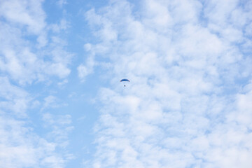 Paratrike with blue parachute flying high in the blue cloudy sky on autumn morning. Paragliding activity. Weekend leisure time and hobby. Extreme sport flight on paramotor machine.