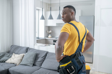 Dark-skinned service man in yellow tshirt standing in the kitchen