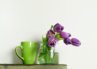 Purple tulips and green cup on light background
