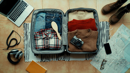 Woman packs winter themed suitcase for autumn holiday. Vacation preparation, careful bag packing. Millennial generation z travel blogger pack suitcase with social media vintage camera, sweater, laptop © BublikHaus