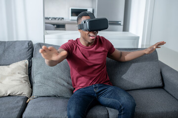 A dark-skinned young man sitting in VR glasses and looking enjoyed
