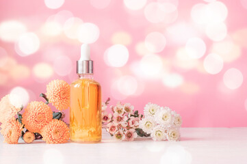 Cosmetic oil among flowers on a pink background. Light bokeh background.