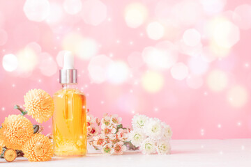 Cosmetic oil among flowers on a pink background. Light bokeh background.