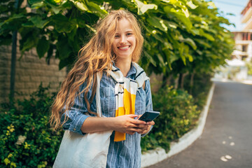 Gorgeous young student female with long blonde hair standing next to the college campus with a...