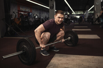 Fototapeta na wymiar Happy handsome athlete smiling to the camera while working out with barbell