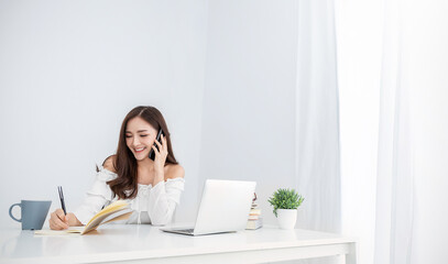 Portrait of young asian business woman talk on smartphone write notebook laptop in home office. Beautiful girl at desk computer take home order. Startup business asia woman online sme telemarketing.