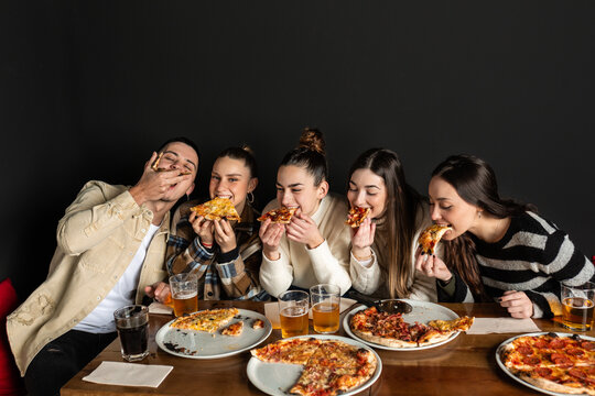 4 Girls And A Boy Bite Into A Piece Of Pizza Having Fun.