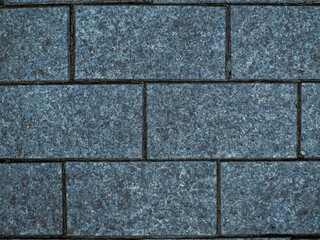 Brickwork of big textured geometric horizontal grey bricks bonded with cement grout between square stones. Wall exterior. Background