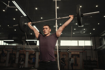 Low angle shot of a strong muscular cross fit athlete lifting heavy barbell overhead