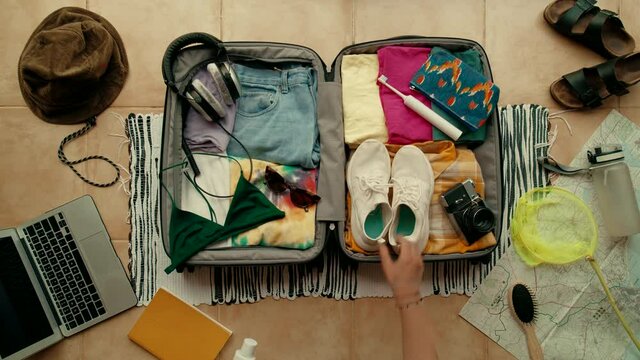 Woman unpacks holiday vacation suitcase in hotel room. Summer bag with bikini swimming suit, running sneakers, camera and colorful happy clothes. International travel blogger