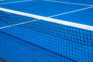Blue tennis court with net. Empty sport field photo. Hard court cover for lawn tennis. Summer sport activity outdoor. White markup on blue court. Sunny day on tennis court. Sport field in park
