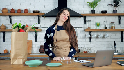 Smiling woman housewife in beige apron listen teacher studying online remote video call conference webcam laptop computer, distance education learning chef cook culinary course in home modern kitchen