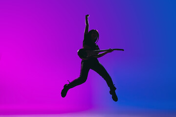 Silhouette of young female guitarist isolated on gradient background in neon.
