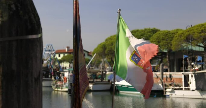 Slightly torn Italian flag waving on one of the moored boats in dock slow motion Caorle Italy