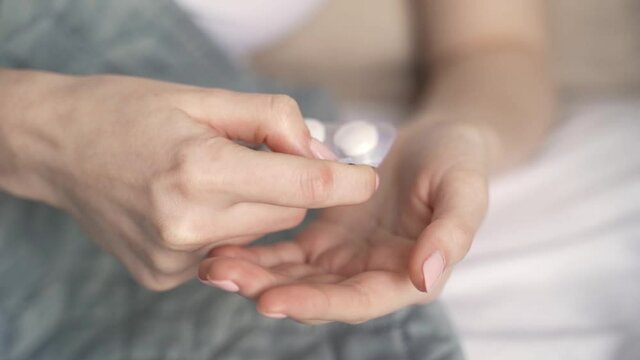 Slow-motion shot of woman hands taking out medicine tablet from a blister pack.