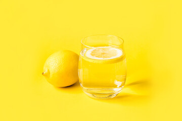 Glass of water with lemon on a yellow background. Summer refreshing drink.
