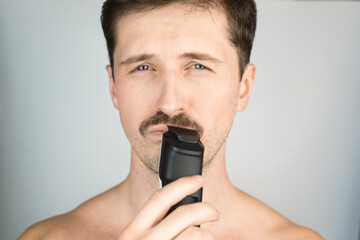 Portrait of man trimming his mustache indoors, close-up. A young mustachioed man with modern...