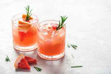 Refreshing grapefruit cocktail with ice and rosemary on a grey background.