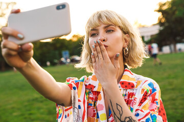 Image of woman taking selfie photo on cellphone and blowing air kiss