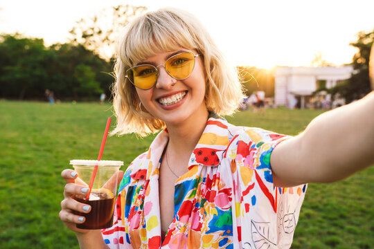 Image of happy young woman taking selfie photo and drinking soda