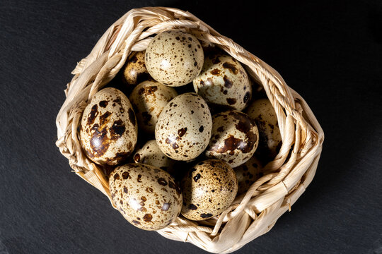 Boiled spotted quail eggs in a wicker basket on black stone plate , isolated on white background. Healthy Food Products Concept