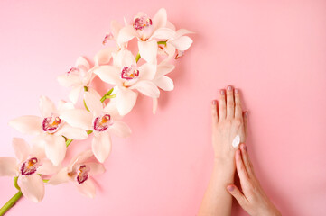Woman applyiing cosmetic cream on her hands on rose background with orhid flower. Home spa, beauty and treatment concept. Flat lay, top view