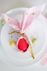 top view of plate with easter egg wrapped in pink napkin shaped like bunny ears