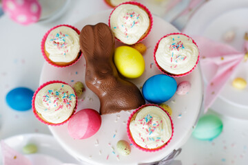 spring holidays concept - close up top view of decorated table with cupcakes, colorful painted eggs and chocolate bunny